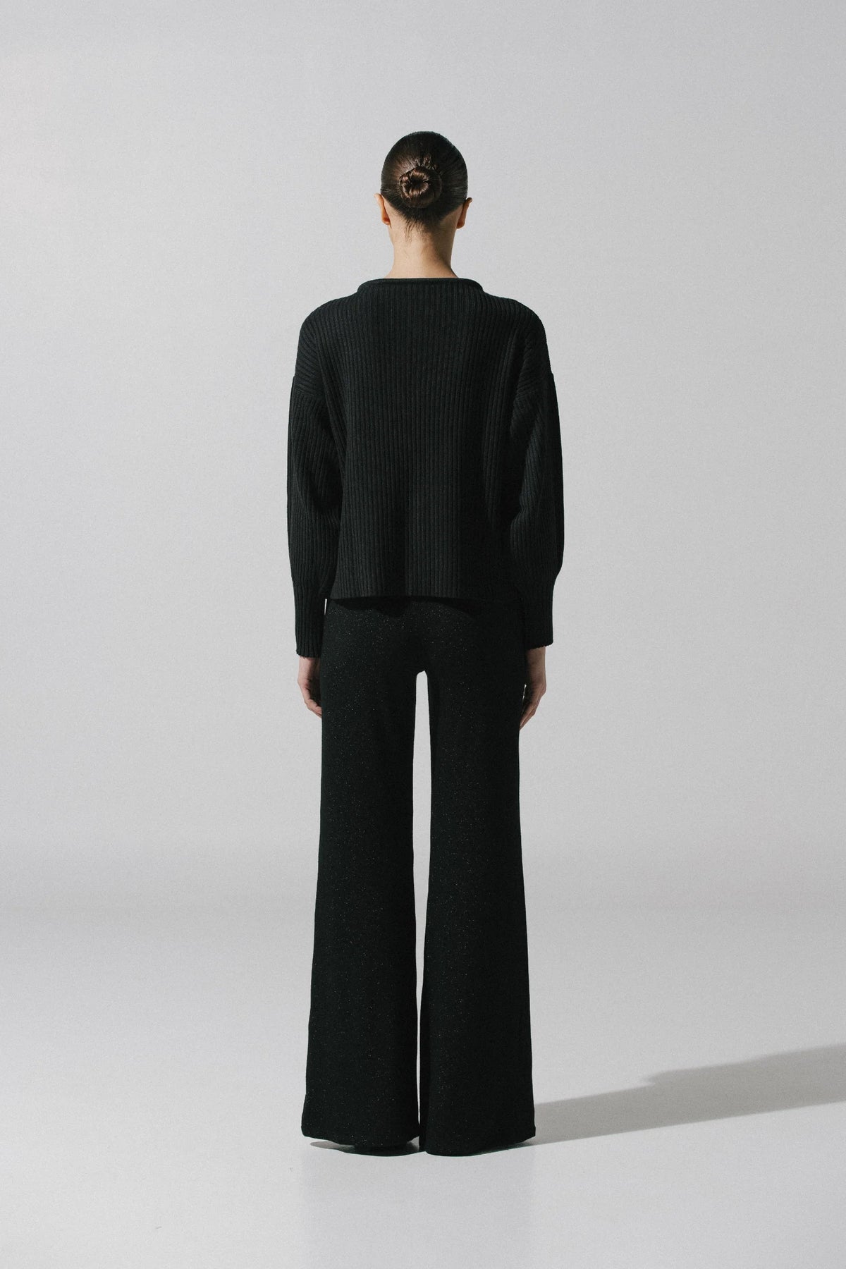 Black Akila Sweater in urban outdoor setting, Ribbed texture and Wide sleeves.