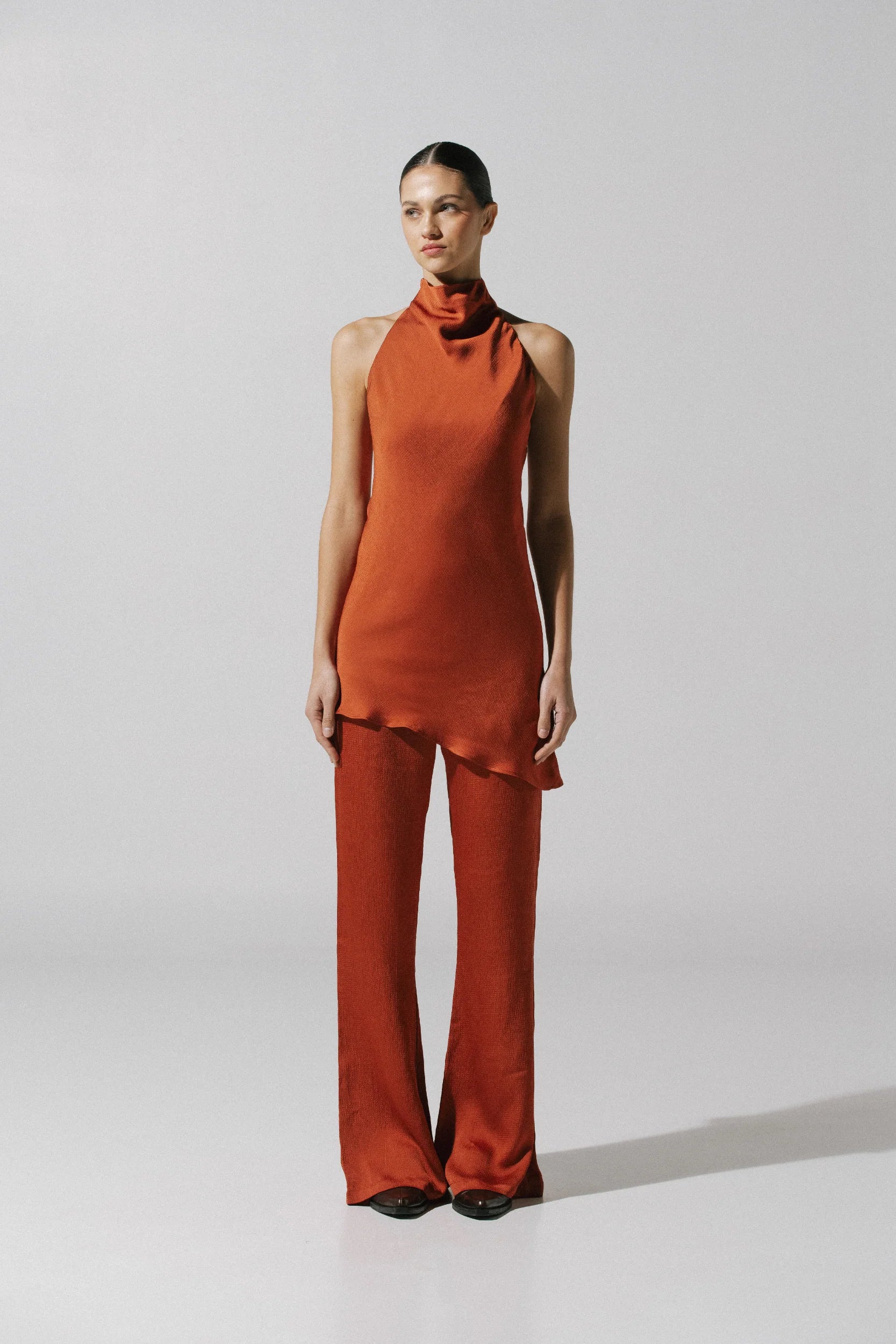 Numa Top by Baobab in terracotta color, Halter Neckline and Asymmetrical hem, paired with pants.