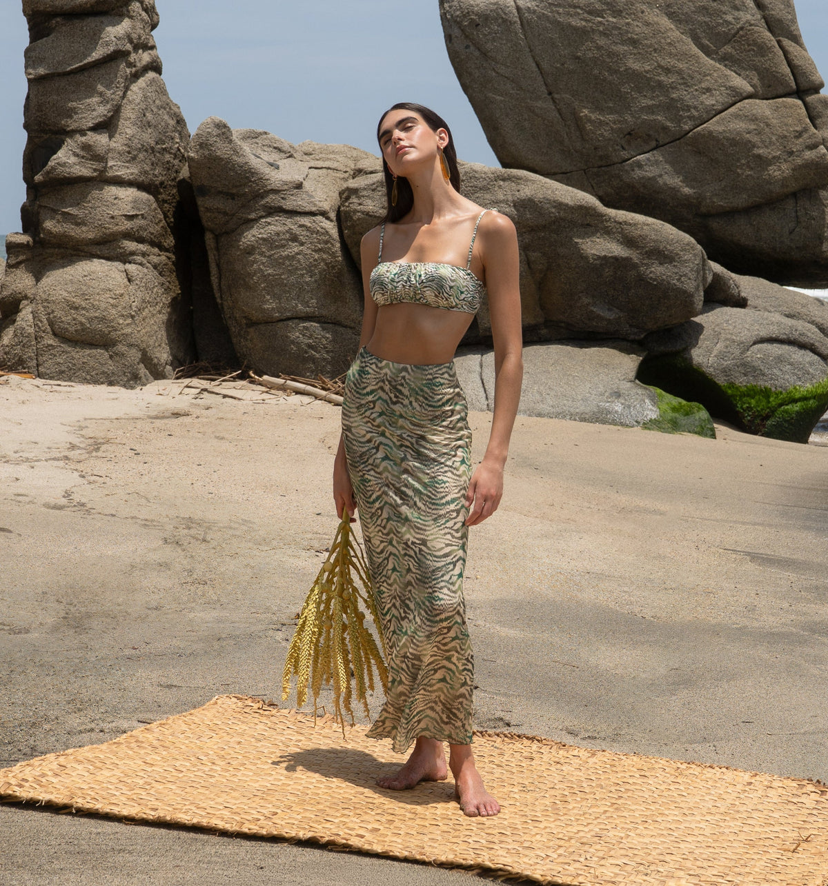 Woman standing on a mat in front of large rock formations on a beach.