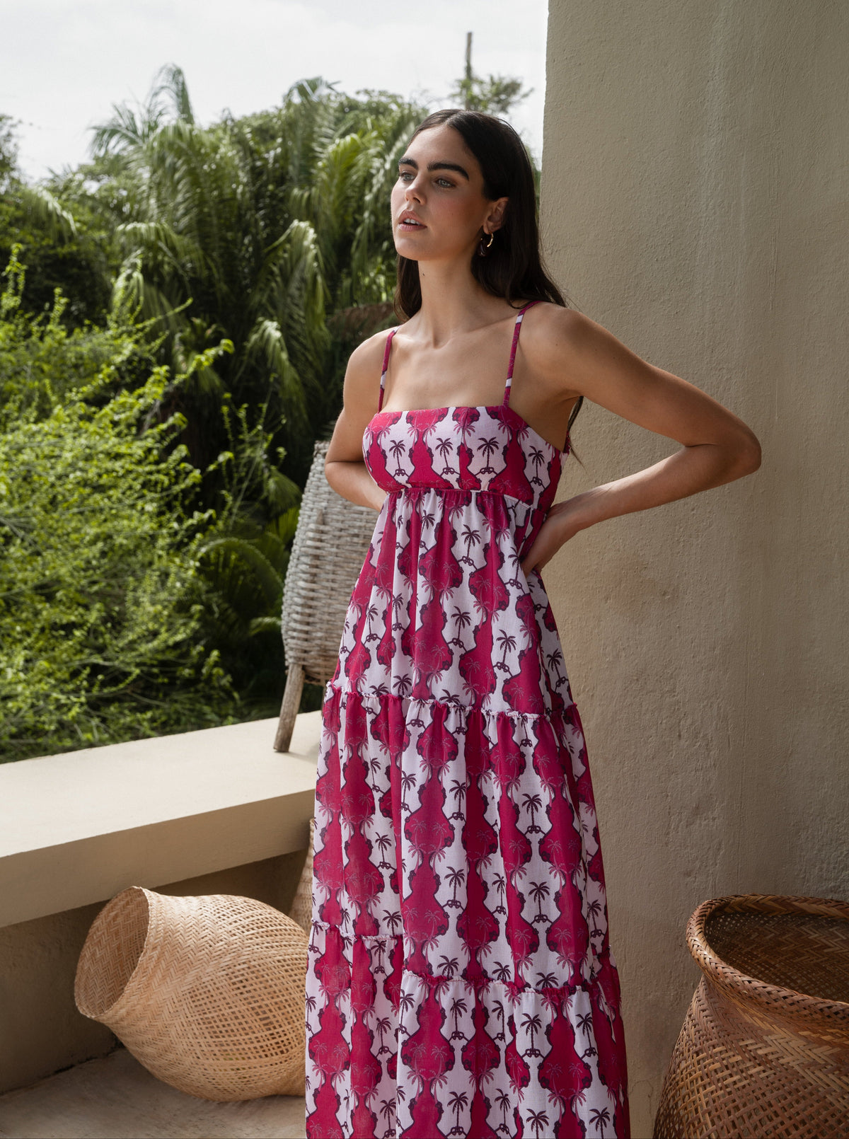 Woman in a pink floral dress standing on a balcony with greenery in the background