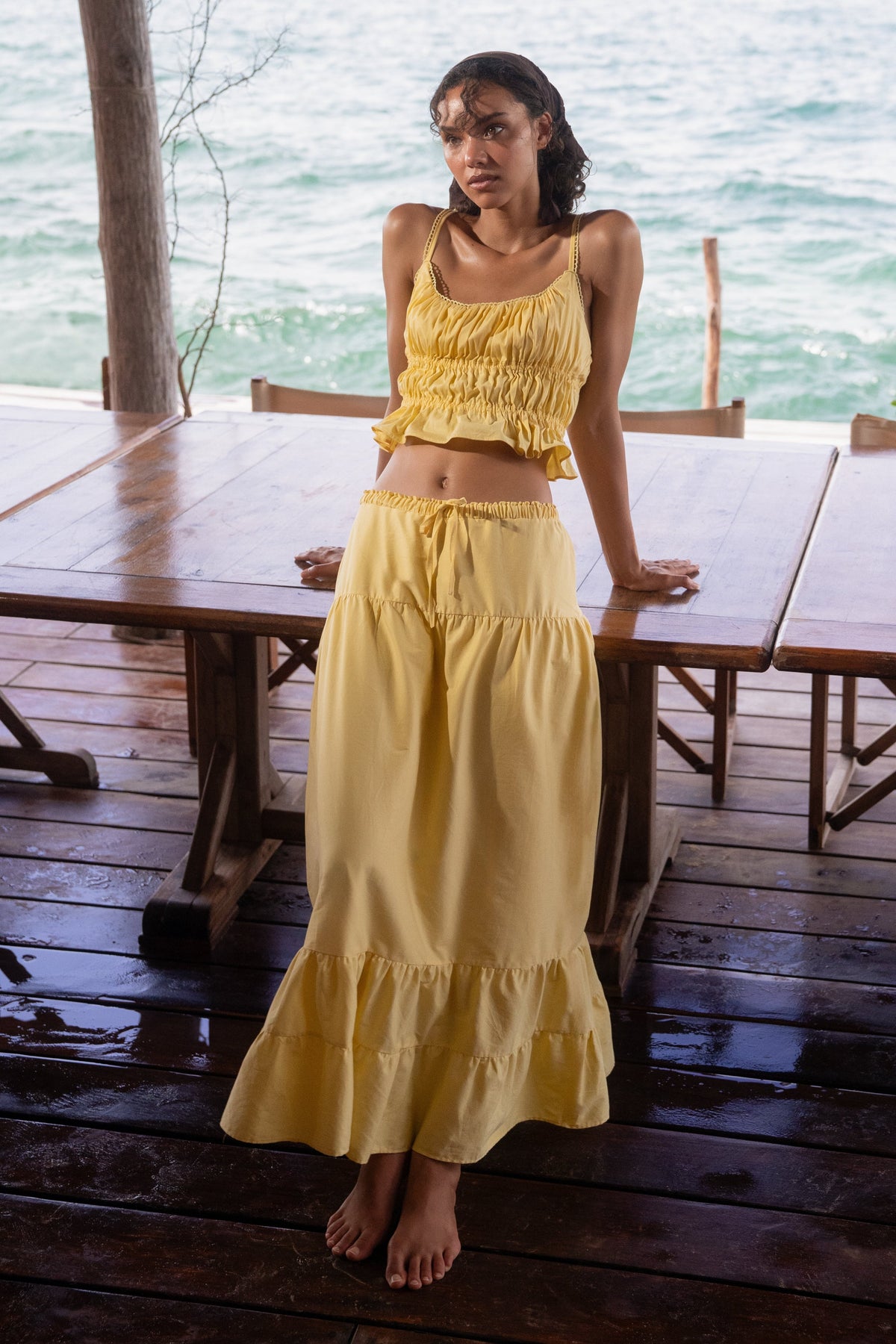 Woman in a yellow outfit sitting at a wooden table by the ocean.
