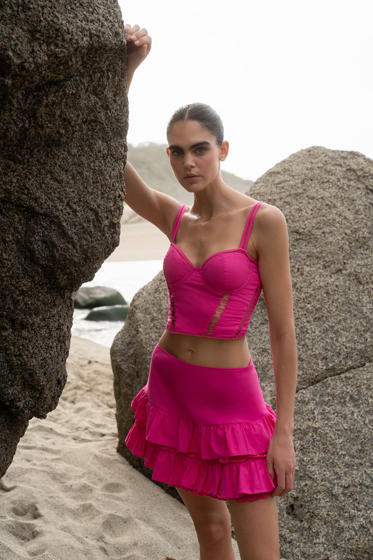 Woman in a pink outfit standing on a beach with large rocks.