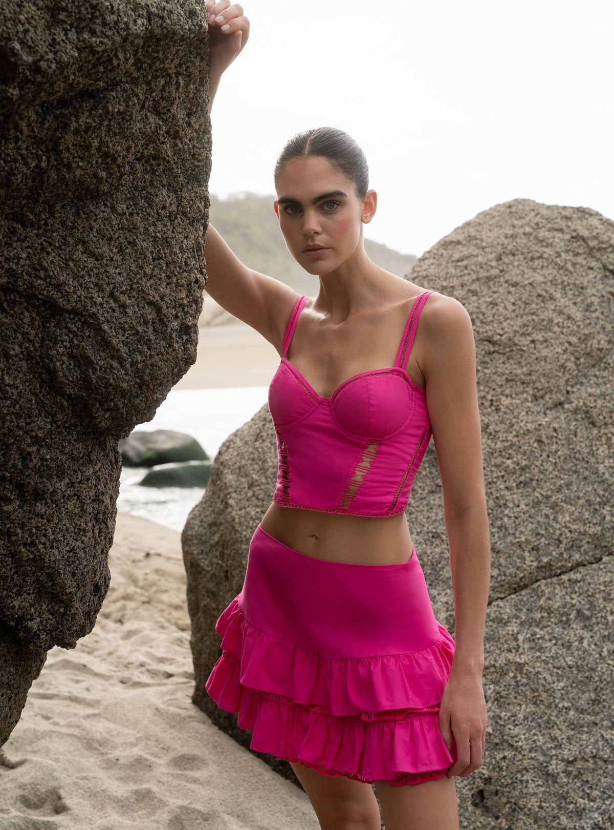 Woman in a pink outfit standing on a beach with large rocks.