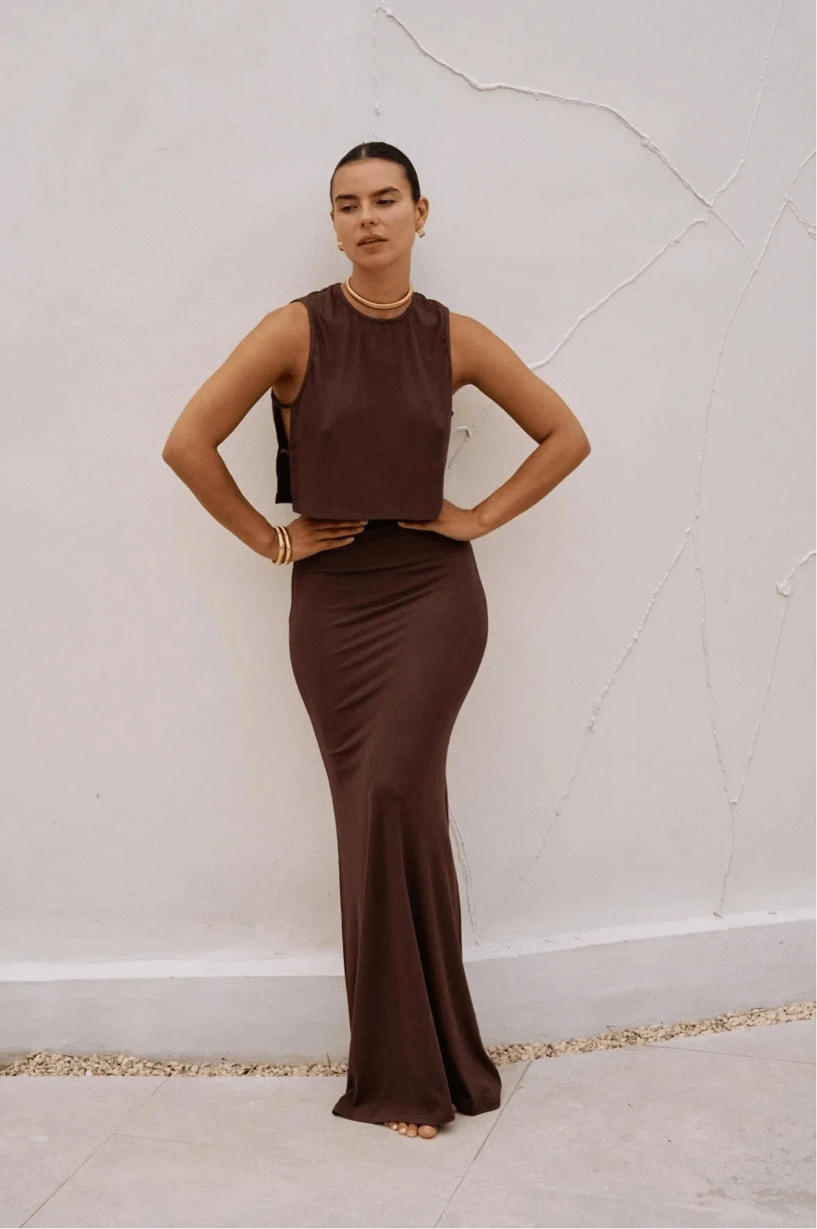 Riot Lounge Dom Maxi Skirt in chocolate color, flowing fabric, high waist, and full length design, showcased on a model.