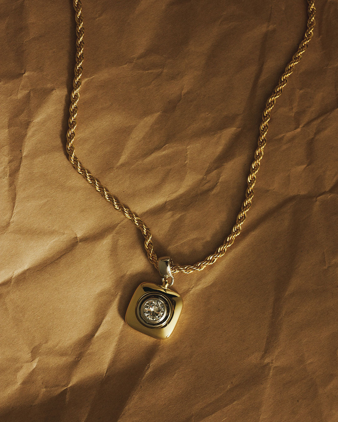 The Luv Aj Luna Bezel Pendant Necklace in Gold on a crinkled paper background