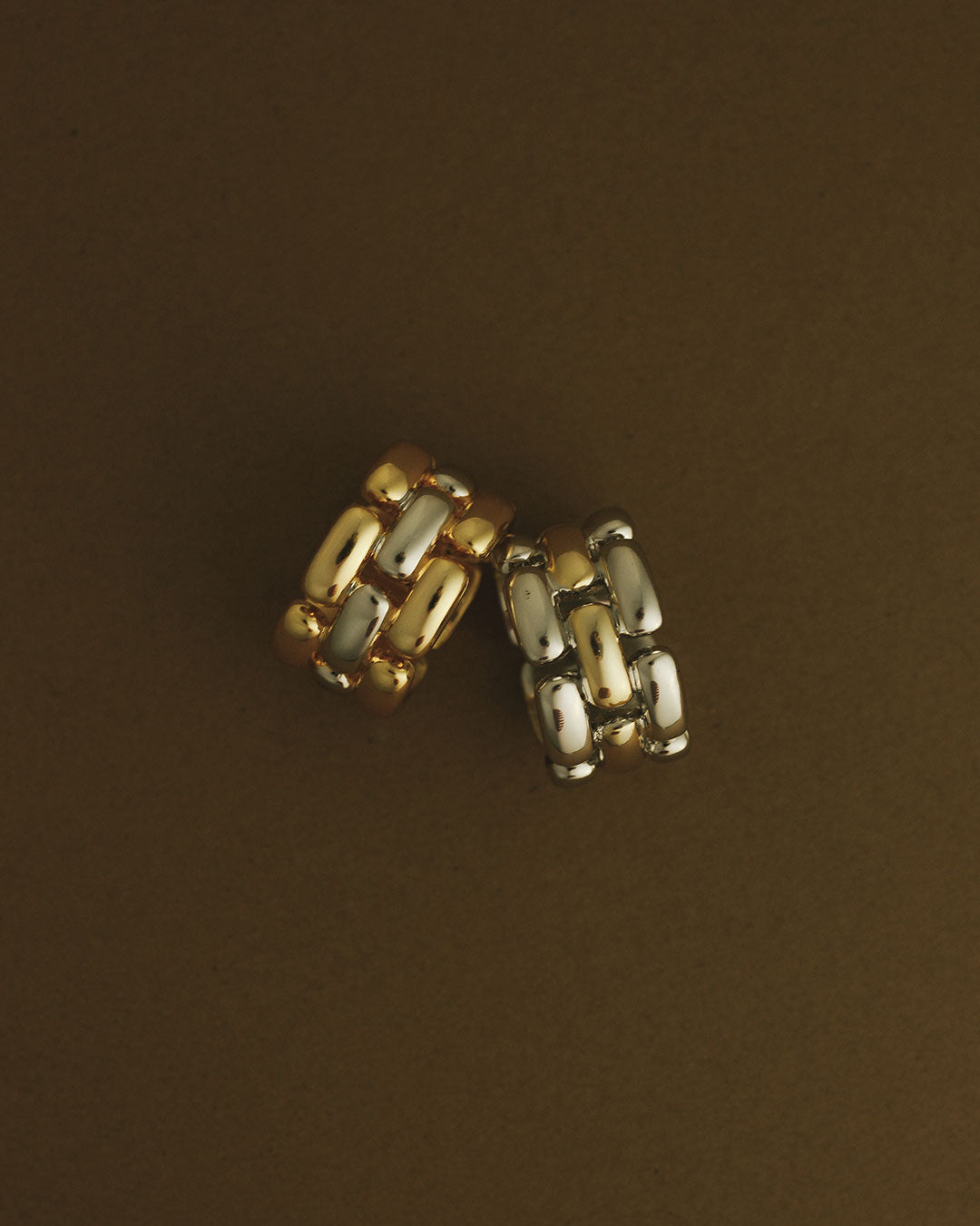 The Luv Aj Noir Link Ring in Silver and Gold in a flat lay photo on a brown background