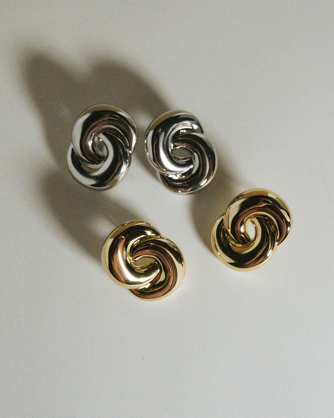 The Luv Aj Soltice Knot Studs in Silver and Gold in flat lay photo