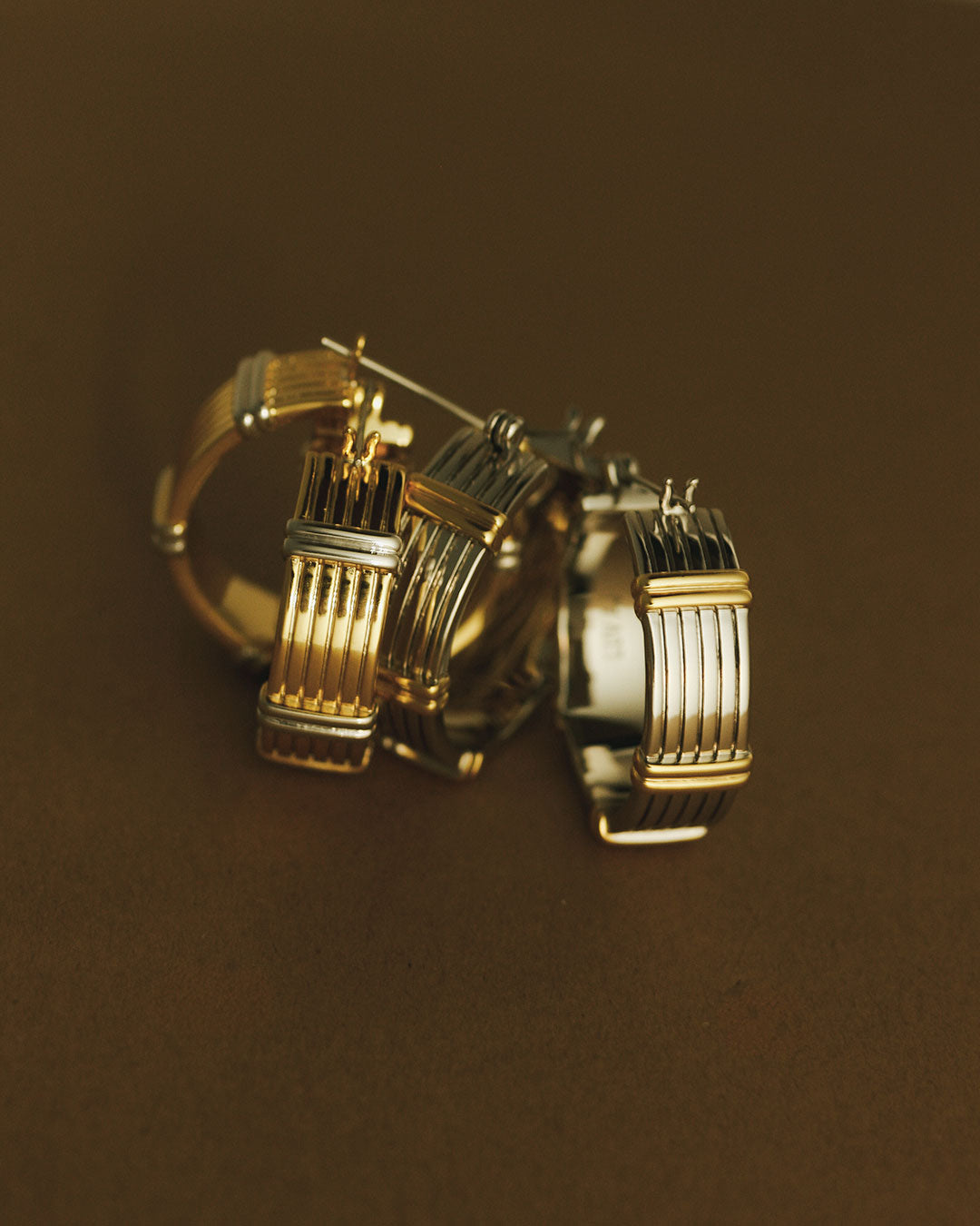 The Luv Aj Two Tone Sierra Bar Hoops in Gold on a brown background
