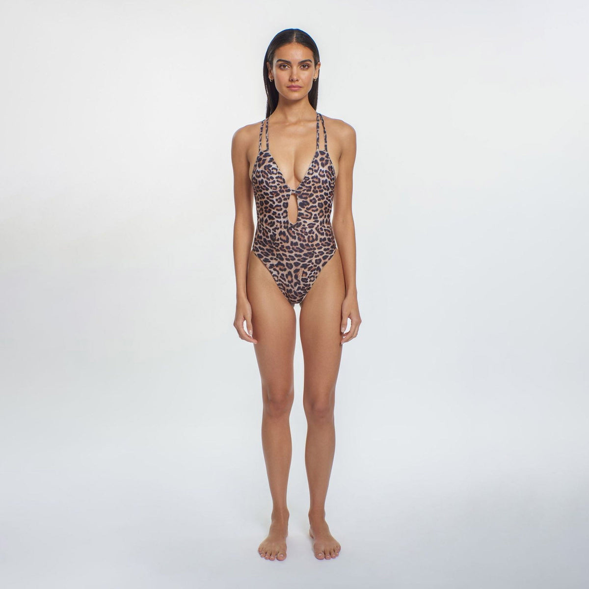 A model wearing a one-piece swimsuit with a 'V' neckline, keyhole cutout, double crisscross straps along the back, and a scrunch detail at the back. The swimsuit has a leopard animal print.